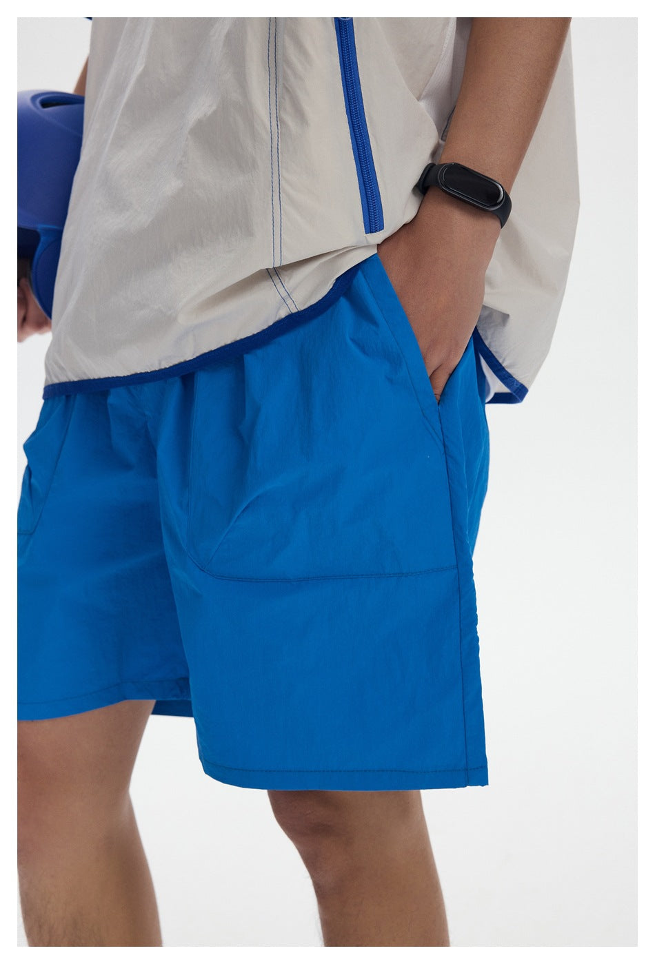 Close-up of bright blue shorts with a large patch pocket, alongside the blue-trimmed hem and zip pocket of the top.