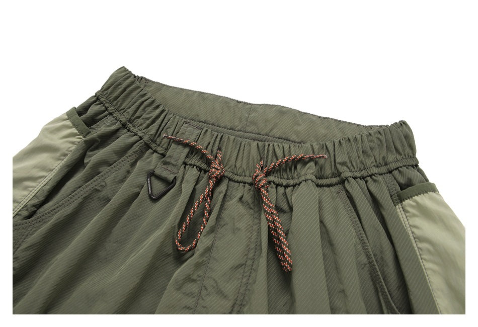 Close-up of olive pants showing the elastic waistband, orange-and-black drawcord, black D-ring and side pocket openings.