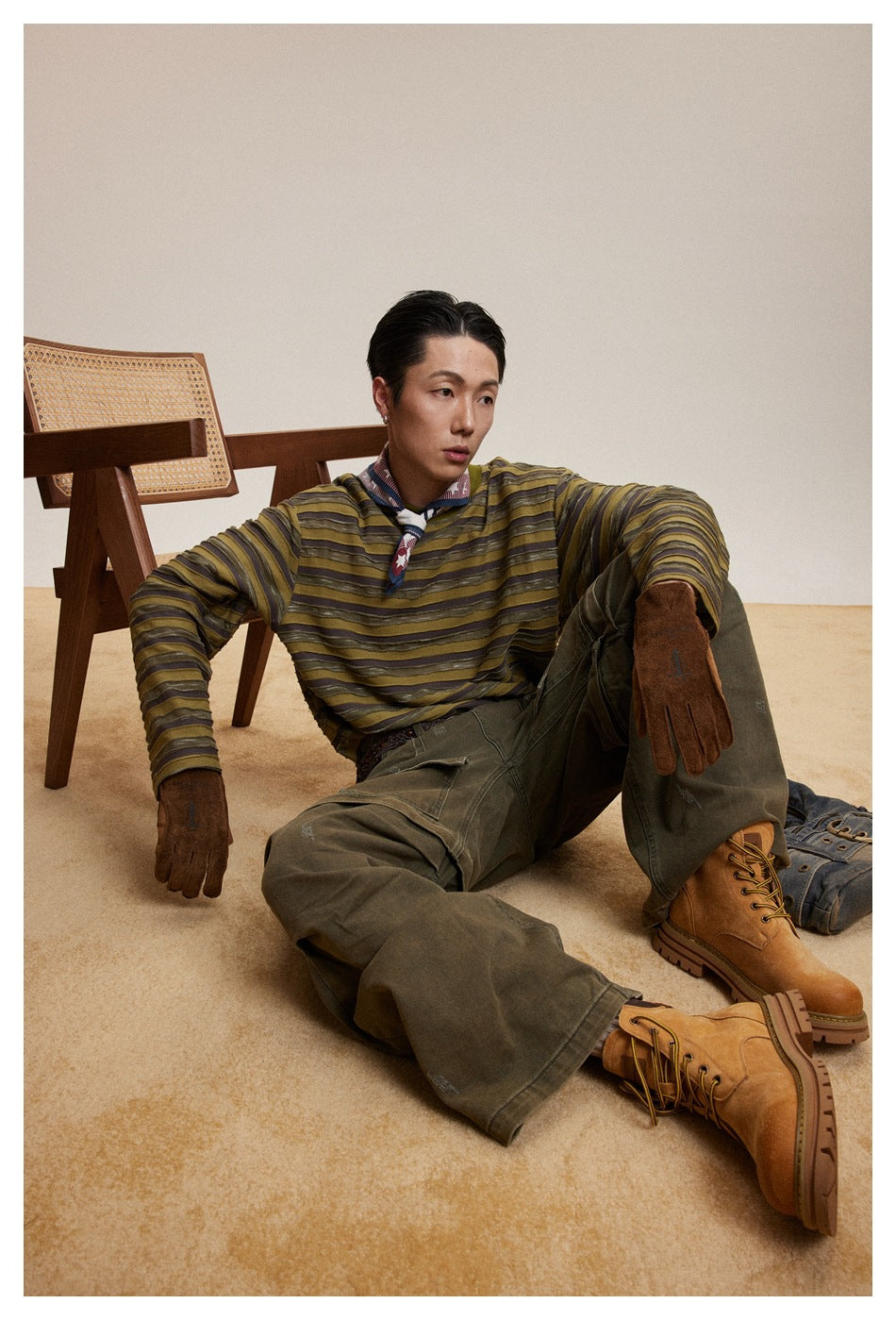 Seated model wearing a black-and-cream striped long-sleeve shirt, brown cargo shorts, and a camouflage cap.