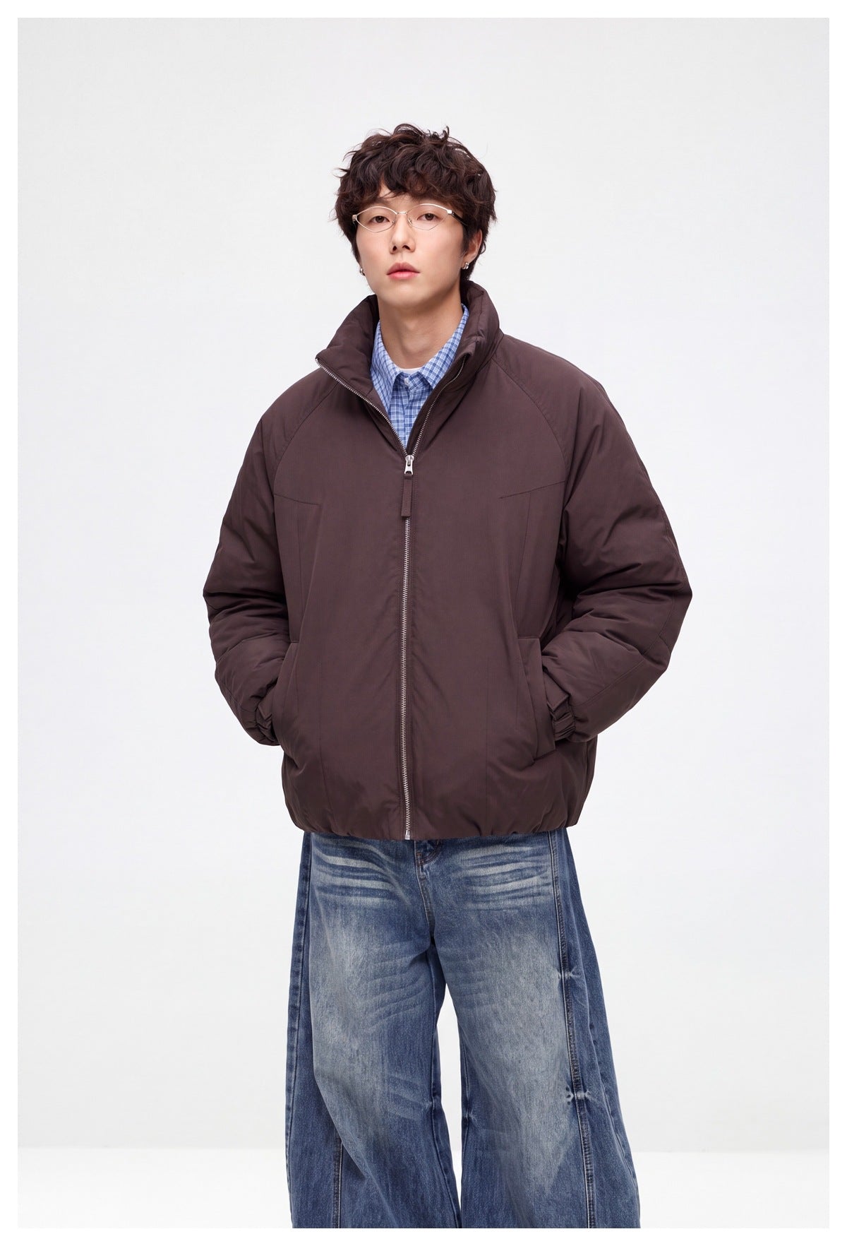 Front view of a model wearing a dark brown padded jacket with a high collar, zip closure and side pockets.