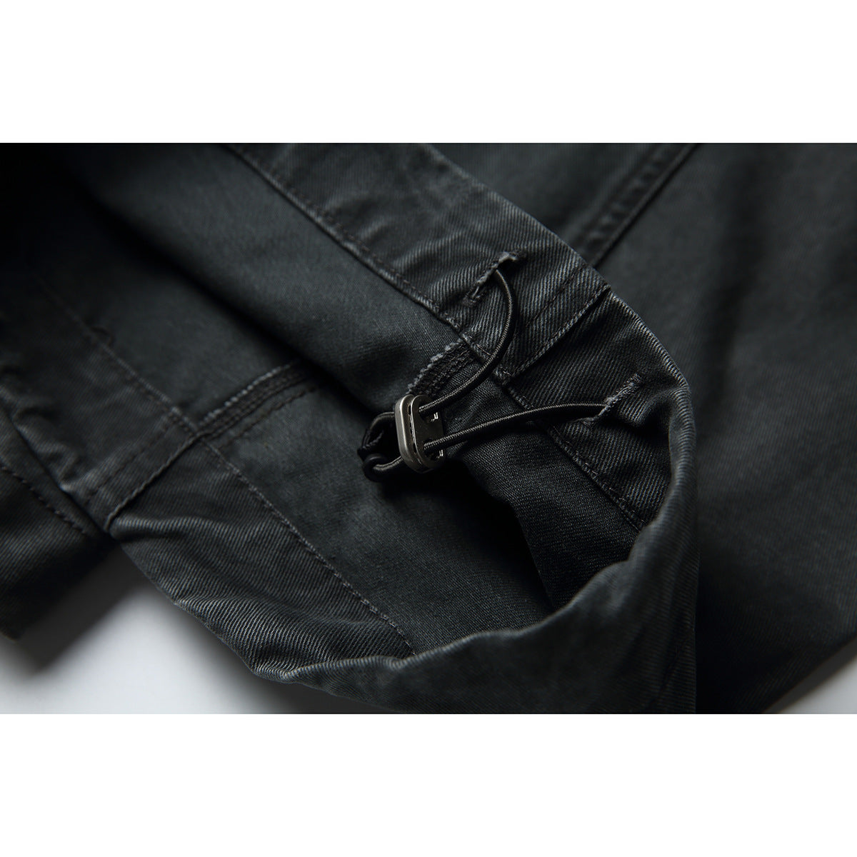 Close-up of charcoal pants showing a small metal buckle and adjustable strap at the garment edge.