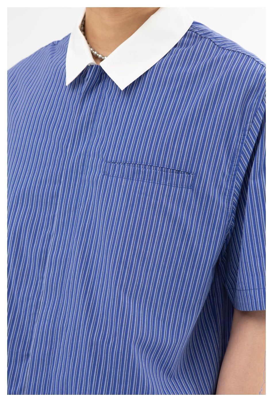Close view of a person wearing a blue shirt with fine vertical stripes, a white pointed collar, and a chest pocket.