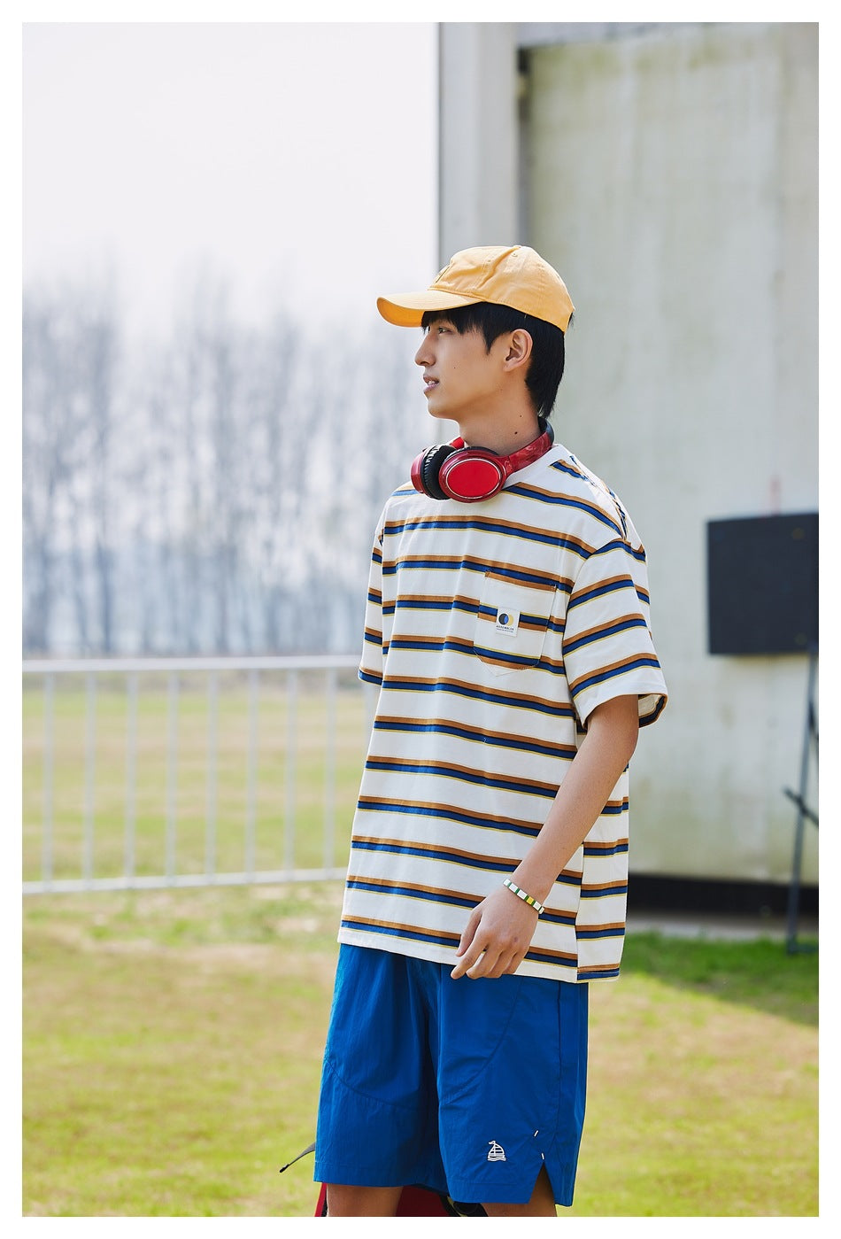 Side view of a model wearing a white T-shirt with navy and mustard stripes and bright blue shorts.