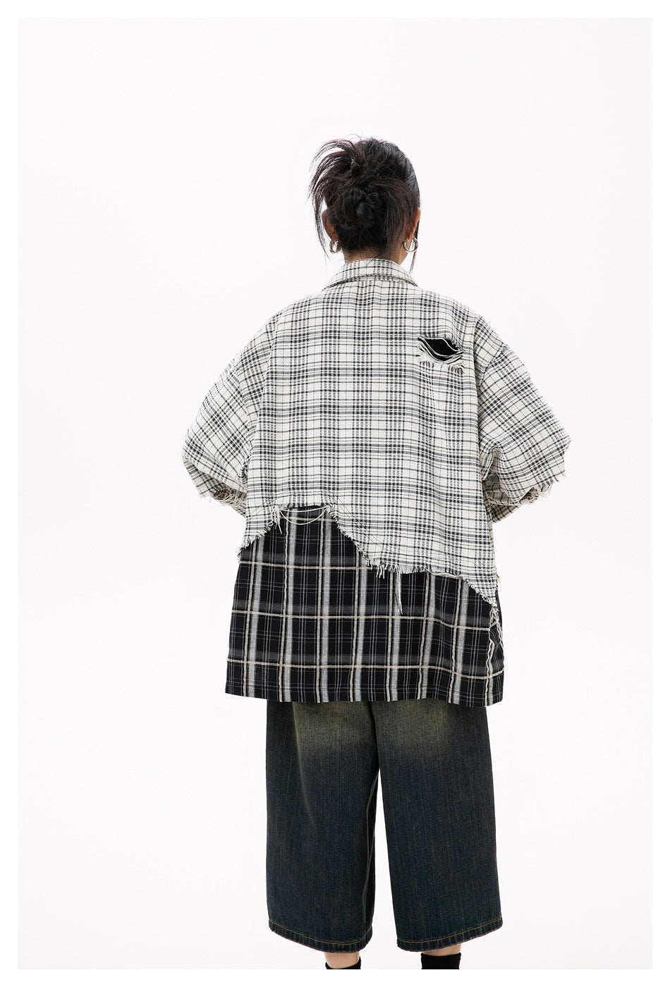 Back view of model wearing the plaid shirt with frayed asymmetric hem and black plaid lower panel with wide-leg denim