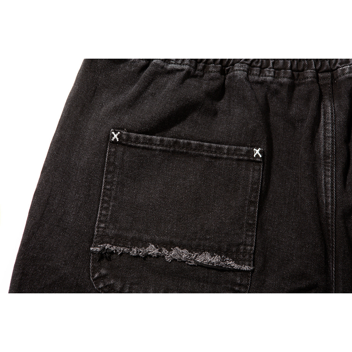 Close-up of a black shorts back pocket with frayed horizontal trim and small white crossed-stitch accents.