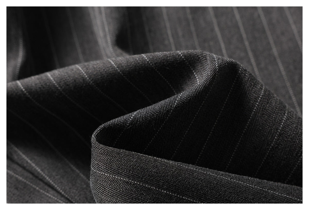 Macro view of folded charcoal pinstripe fabric showing its woven texture and narrow light stripes.