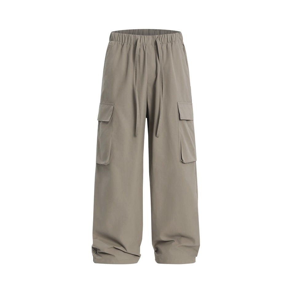 Front view of loose taupe cargo pants with an elastic drawstring waist and large flap side pockets.