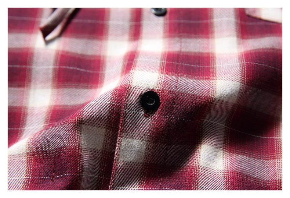 Close-up of a black button and stitching on red, burgundy, and cream plaid fabric.