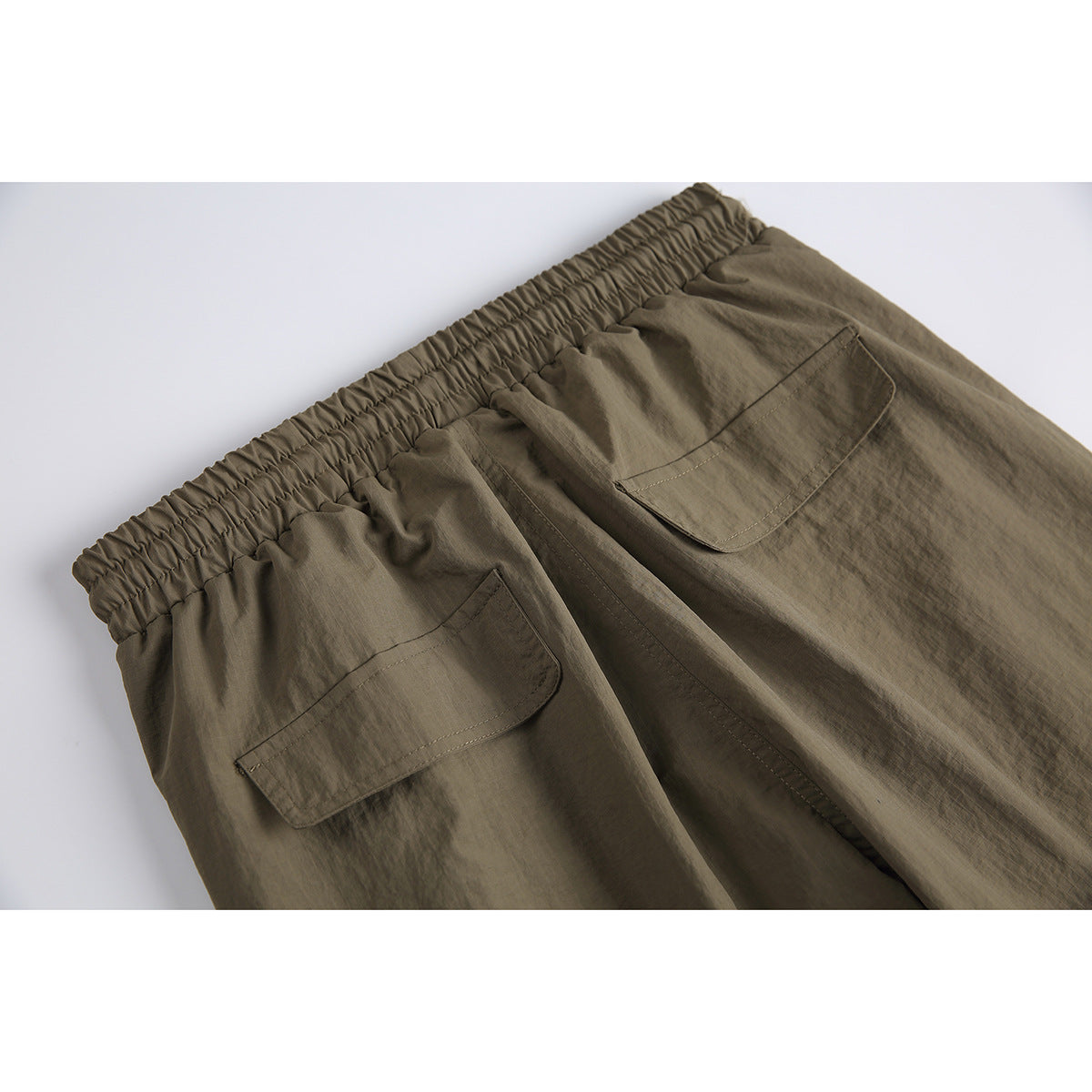 Close-up of the olive-brown pants' gathered elastic waistband and two rear flap pockets.