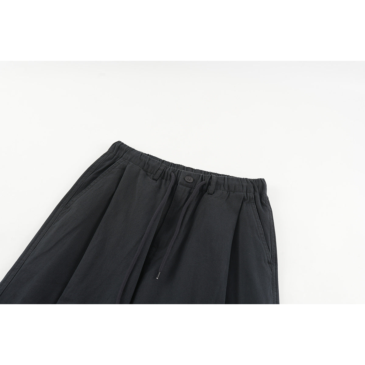 Close-up of black wide-leg pants showing the elasticated waistband, button, drawstring and front pleats.