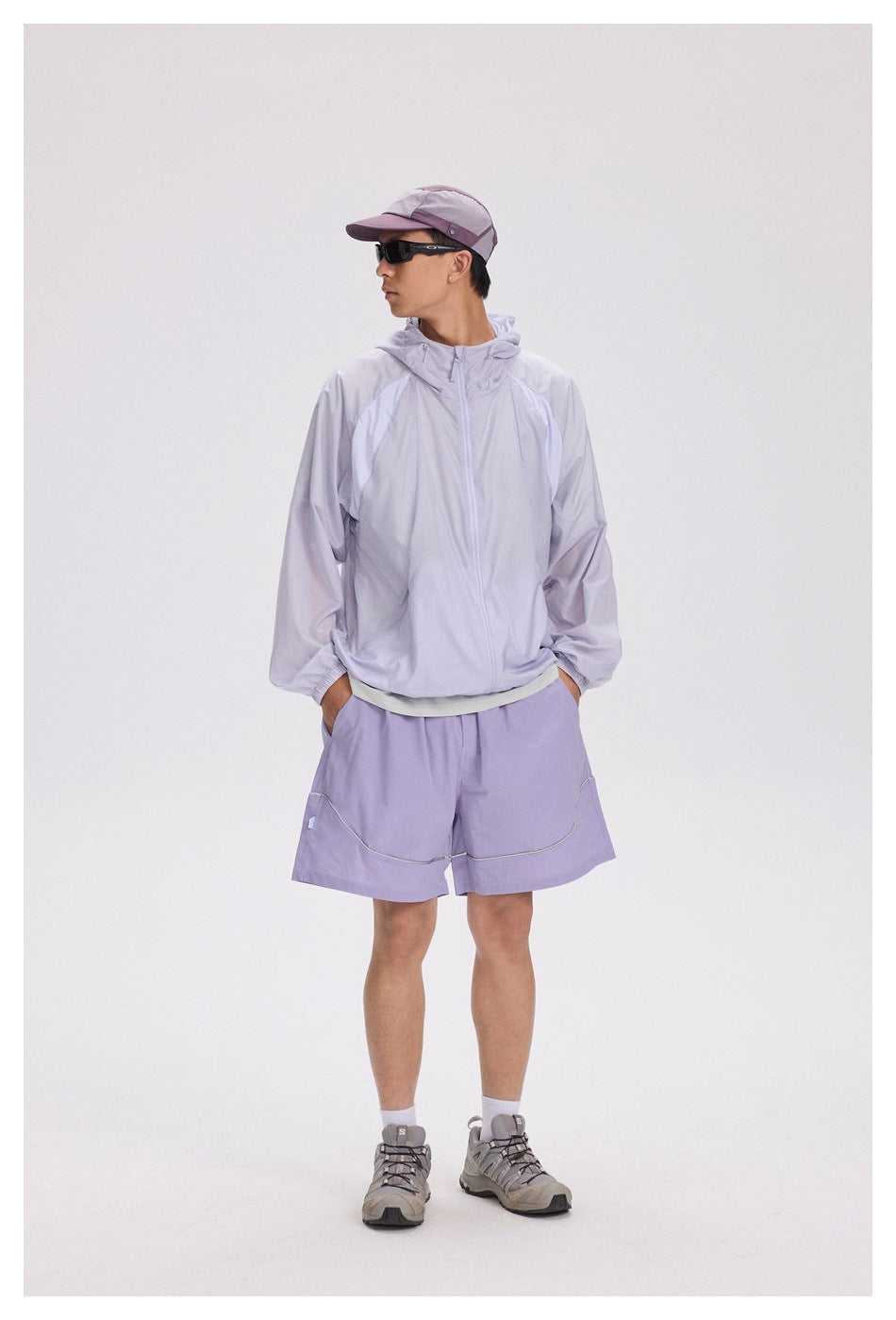 Full-length model wearing a pale lavender hooded zip jacket with matching shorts and a color-block cap.