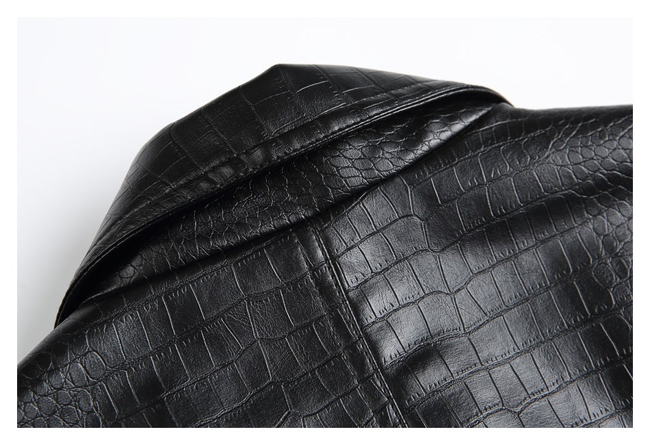 Close-up of a folded, overlapping section of glossy black crocodile-embossed garment fabric.