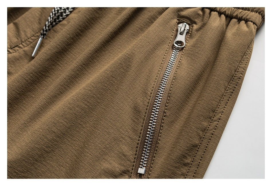 Close-up of a silver zipper and stitching on tan shorts, with part of the drawstring visible.