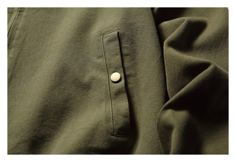 Close-up of an olive jacket's narrow pocket tab with a round metal snap.