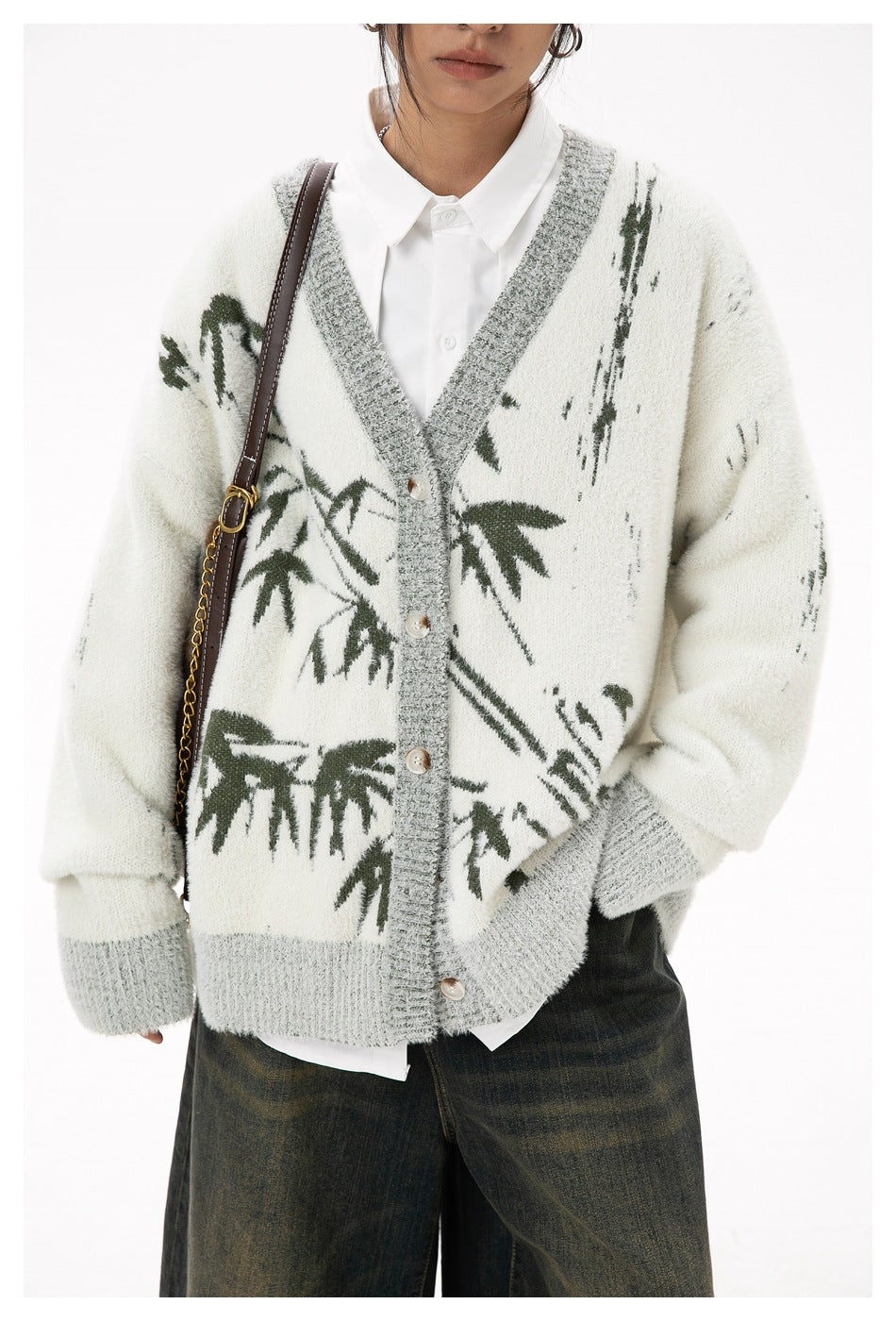 Cropped view of a model wearing an ivory cardigan with gray ribbed edges, buttons, and dark green botanical motifs.