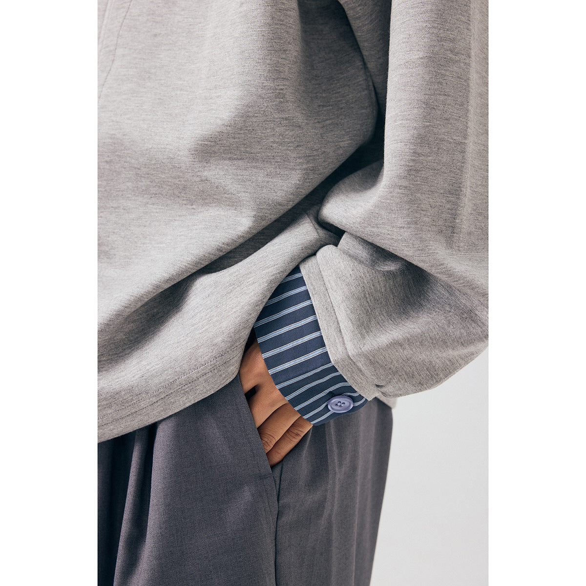 Close-up of the gray jacket sleeve and striped shirt cuff, with a button and loose charcoal trousers visible.