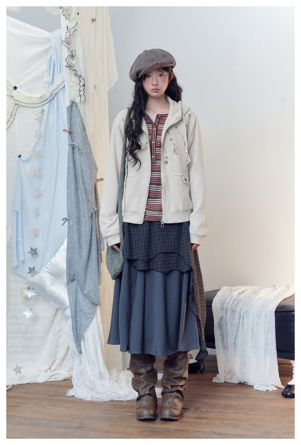 Model wearing a cream zip hooded jacket with star and moon embroidery over a striped top, long skirt and brown boots