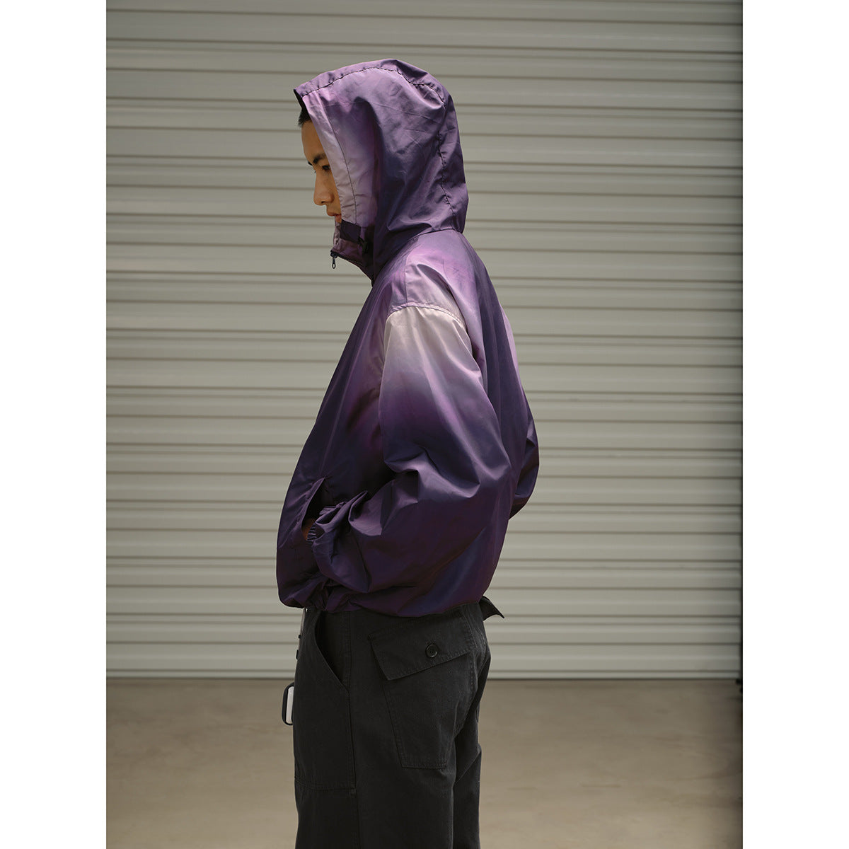 Side view of a man wearing a purple hooded jacket with elastic cuffs and black cargo trousers.