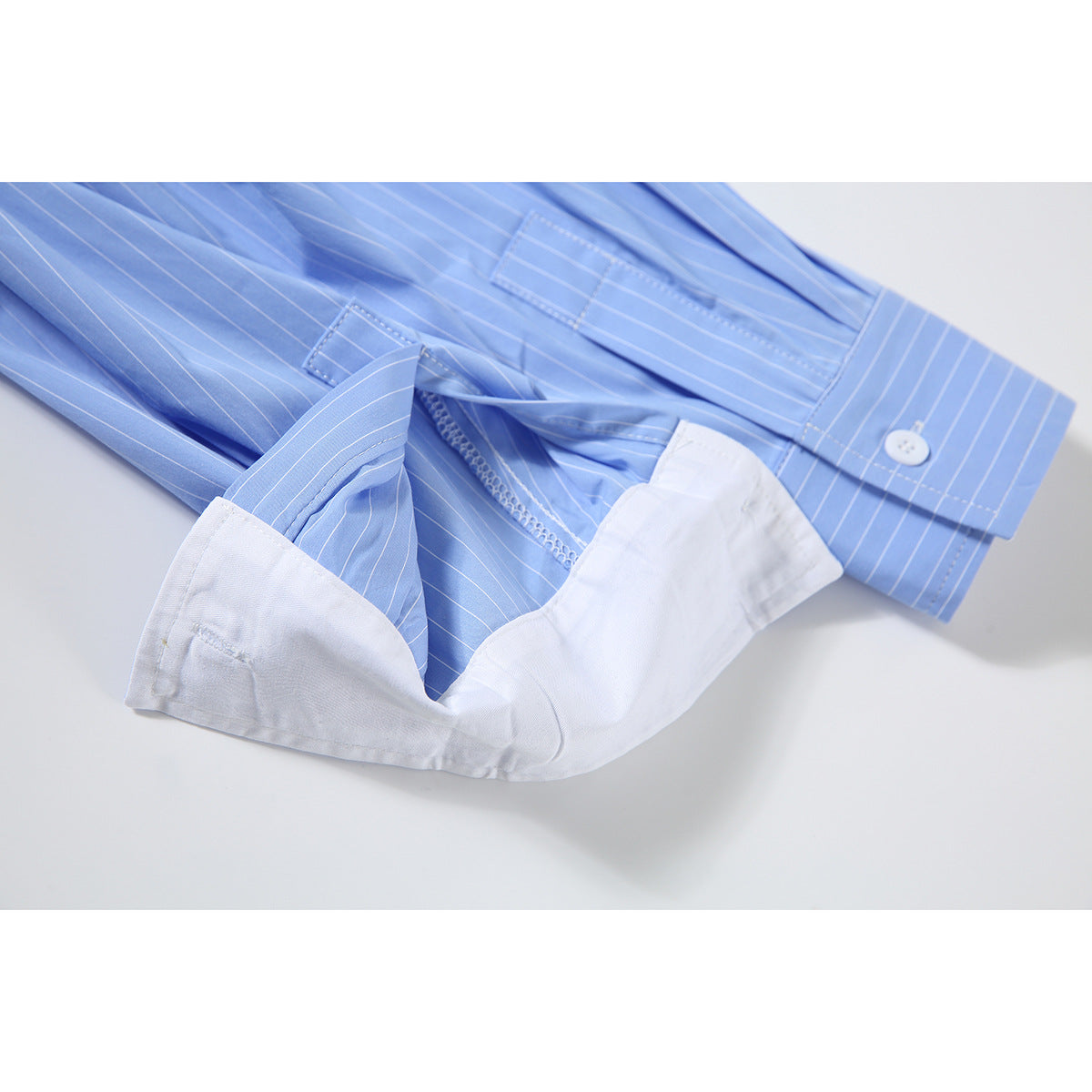 Close-up of the white cuff and button on a light blue pinstriped shirt.
