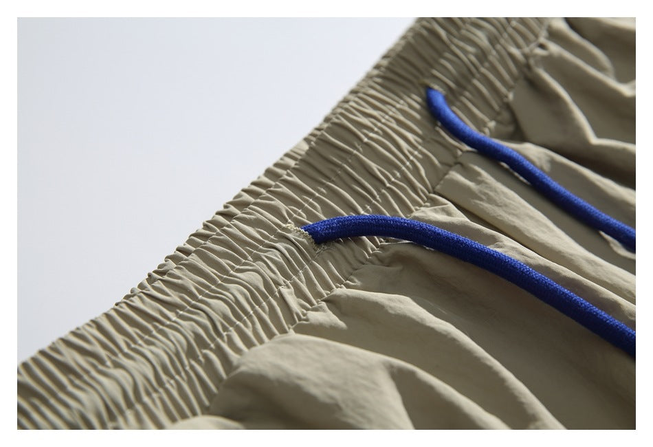 Close-up of beige trousers with a gathered elastic waistband and bright blue drawcords.