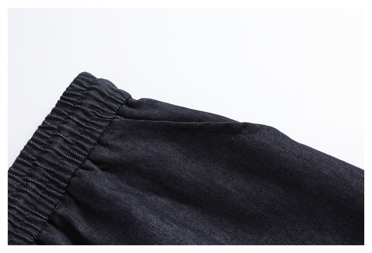 Close-up of the gathered elastic waistband and upper fabric of dark indigo pants.