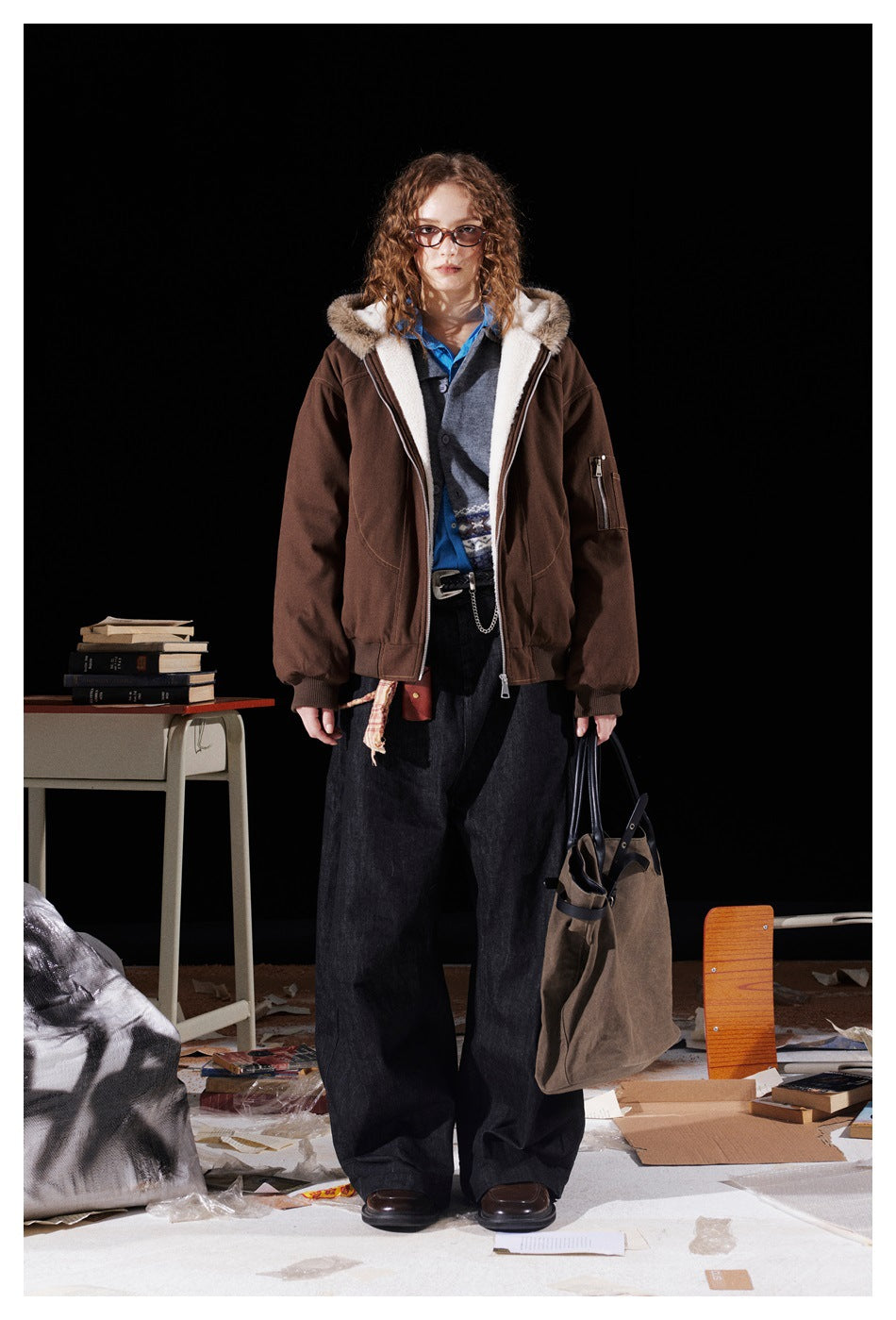 Full-length front view of a model wearing an open brown jacket with cream lining, a fur-trimmed hood, and dark wide trousers.