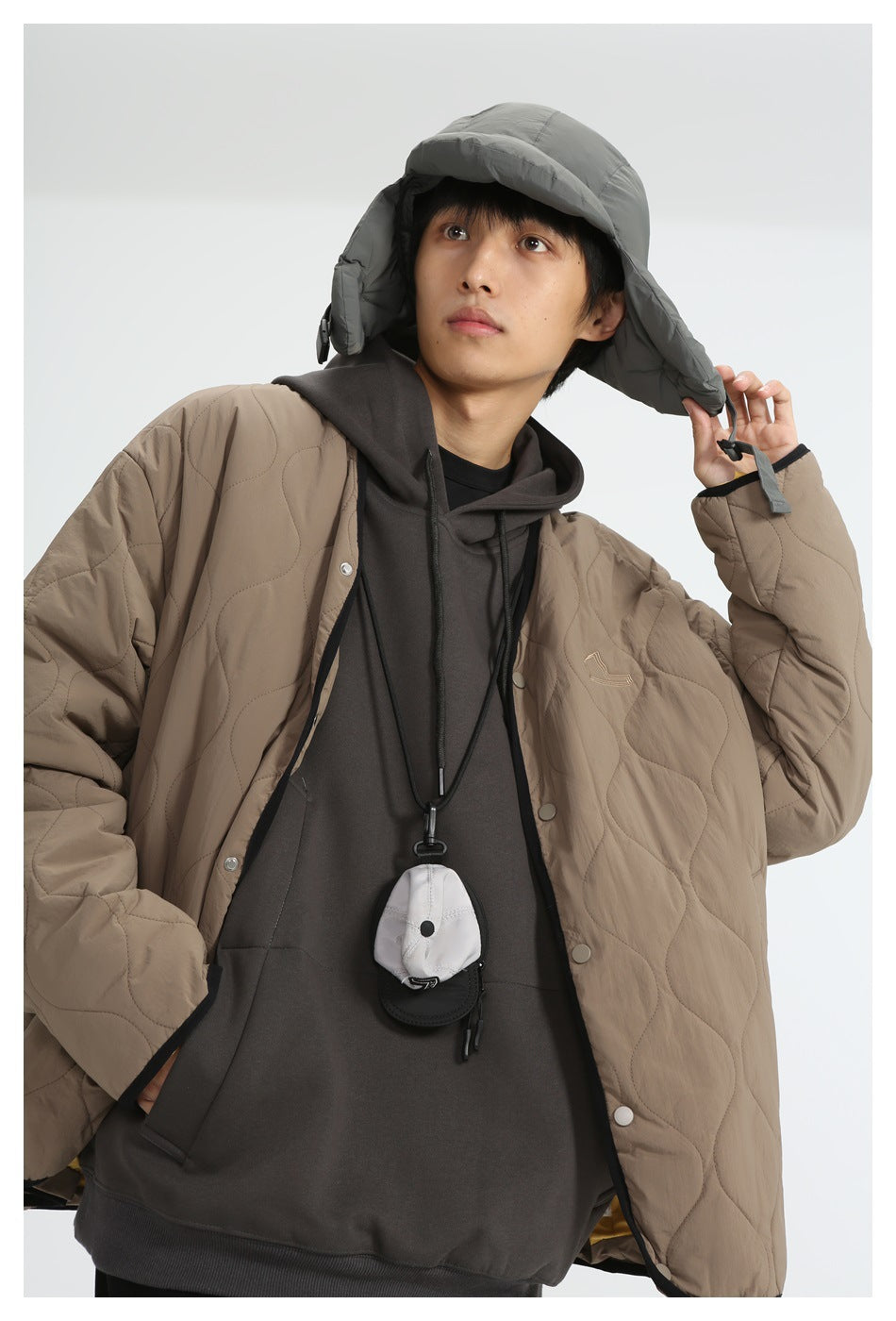 Model wearing brown quilted snap-front jacket over a gray hoodie with a gray padded hat