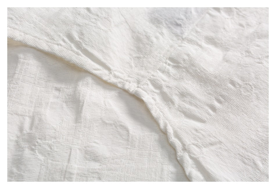 Extreme close-up of white textured fabric, showing its raised woven pattern and a folded edge.