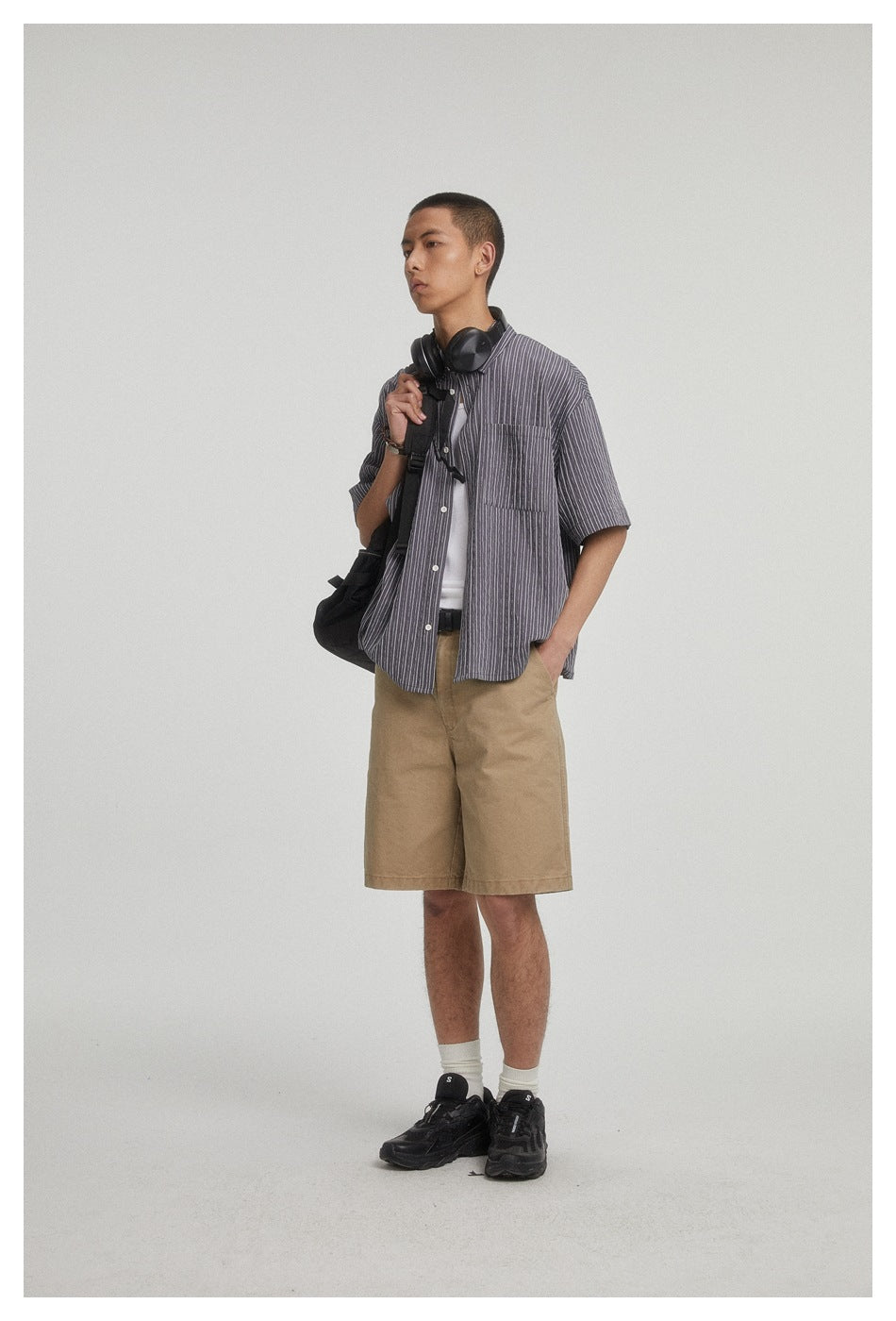 Model wearing a charcoal gray pinstriped short-sleeve button-up shirt over a white top and tan shorts.
