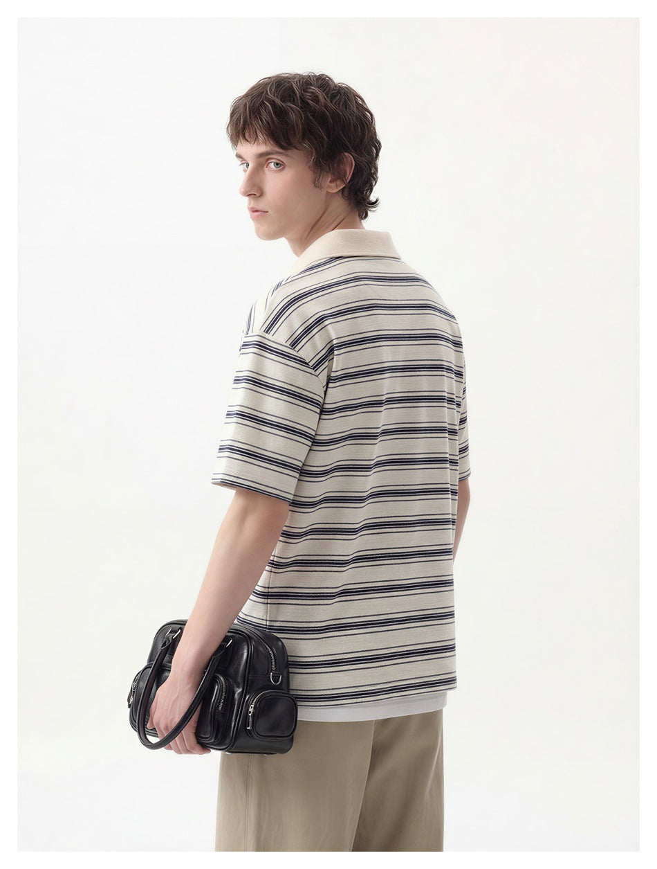Rear three-quarter view of a man wearing an ivory polo with dark horizontal stripes and beige trousers.