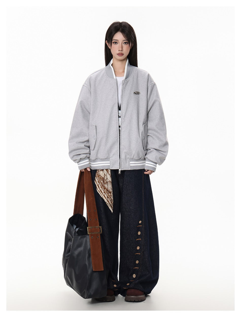 Model wearing a gray bomber jacket, zipped, with dark wide-leg jeans and a large black bag with a brown strap