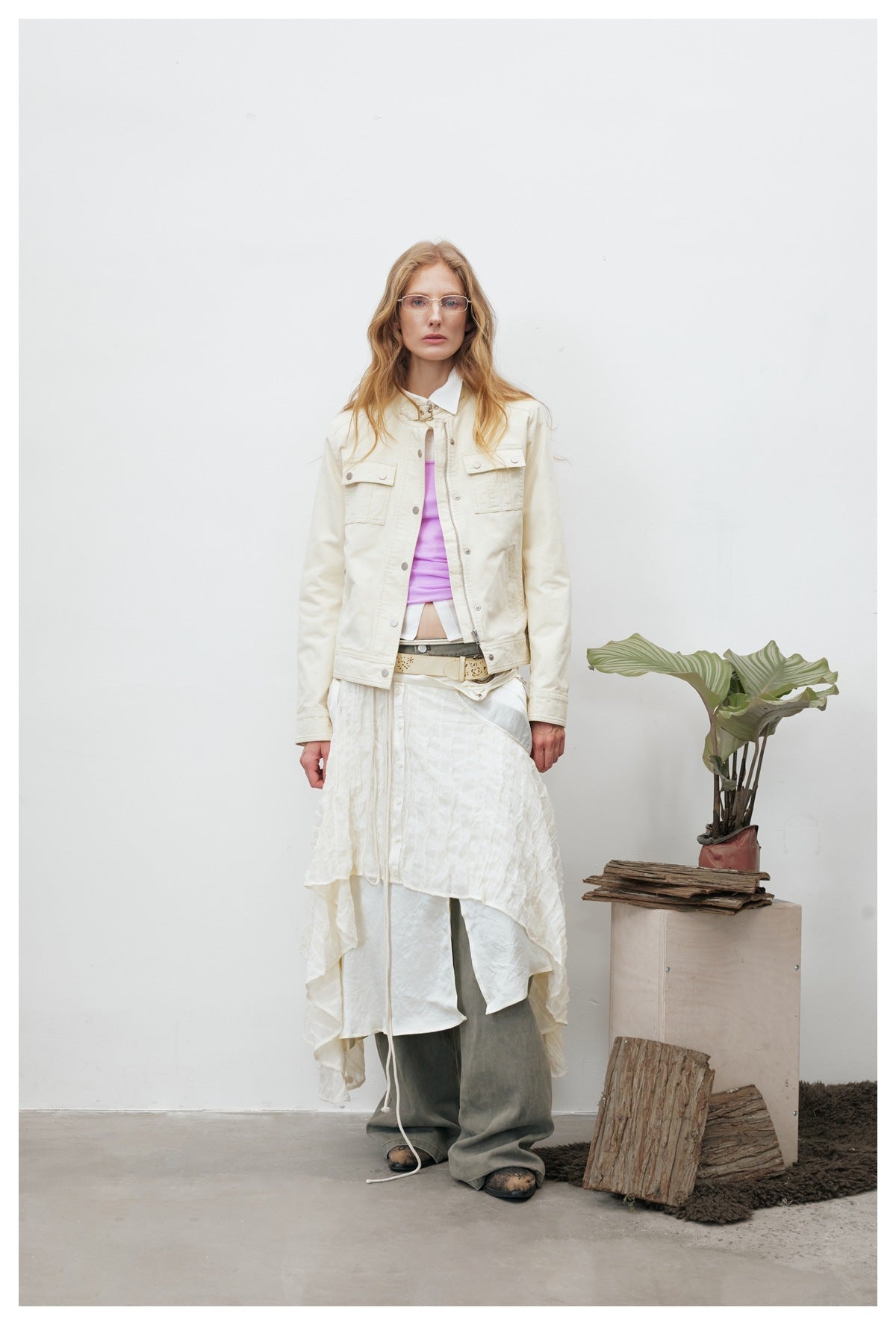 Model wearing an off-white cropped jacket with chest flap pockets over a lilac top, layered skirt and wide olive pants