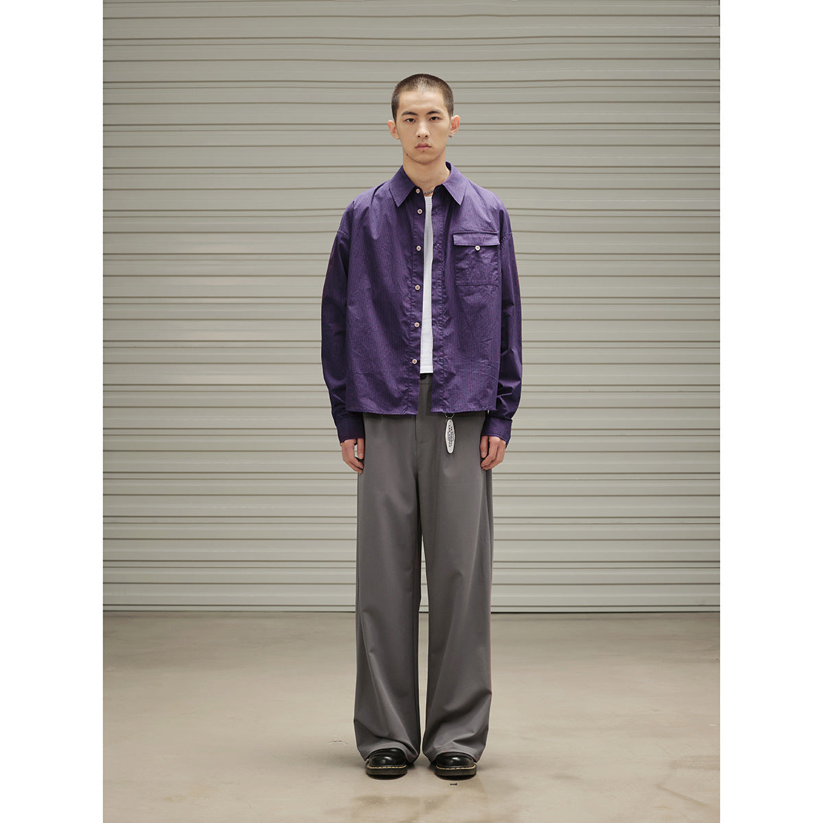Front view of a model in a purple button-up overshirt, white T-shirt, and wide gray trousers.
