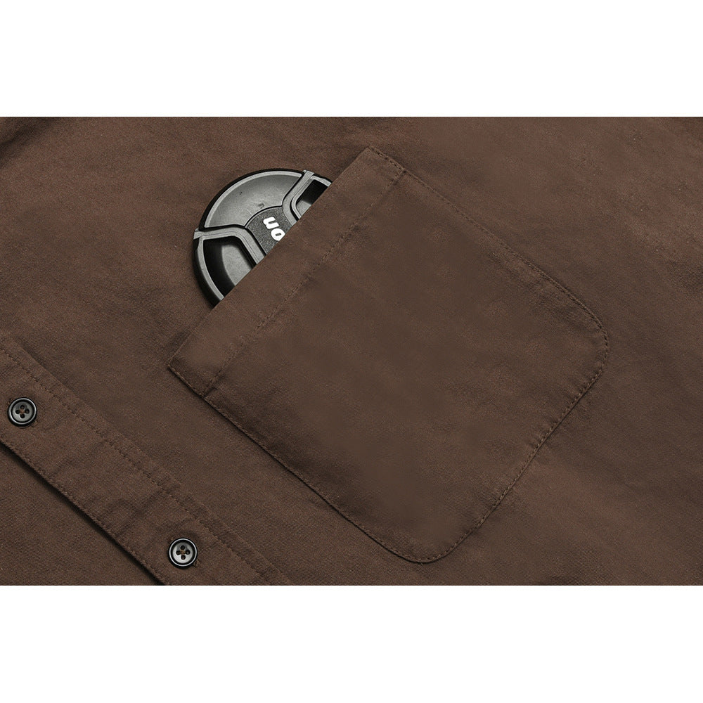 Close-up of a brown shirt’s chest pocket and placket, with part of a dark round object tucked inside.