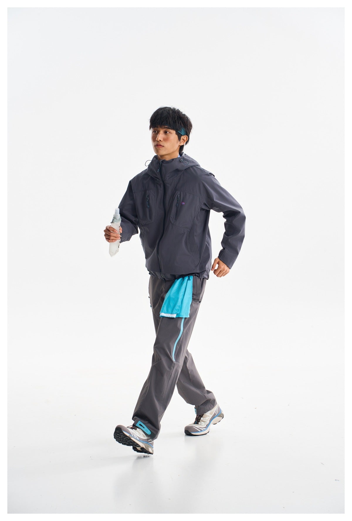 Model walking in a charcoal hooded jacket and matching trousers with bright turquoise accents.