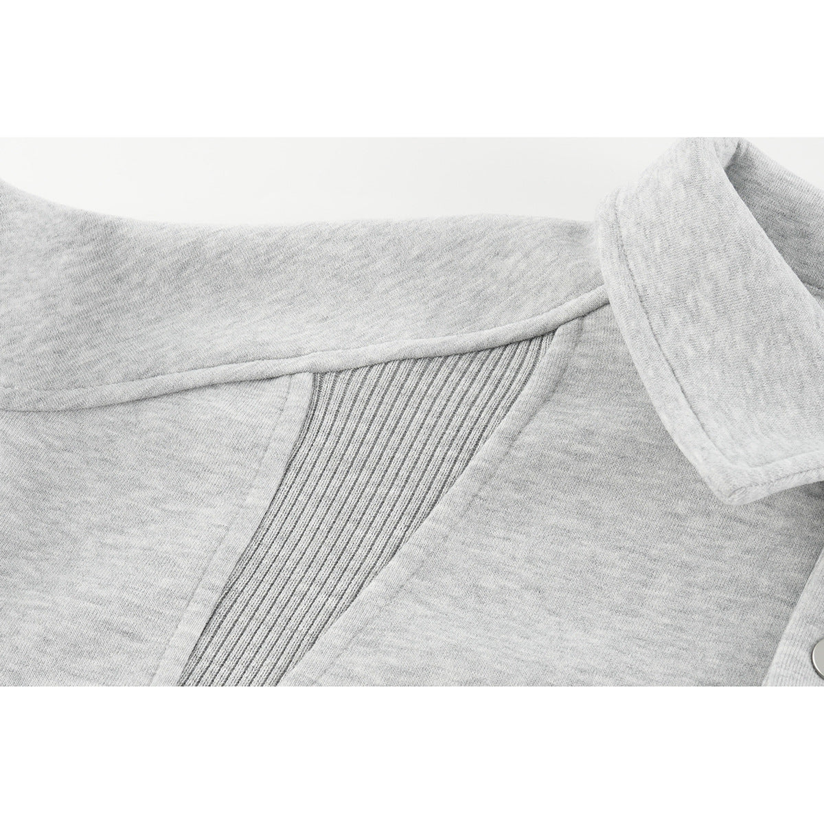 Close-up of the light gray sweatshirt's ribbed shoulder panel, collar edge, and a silver snap.