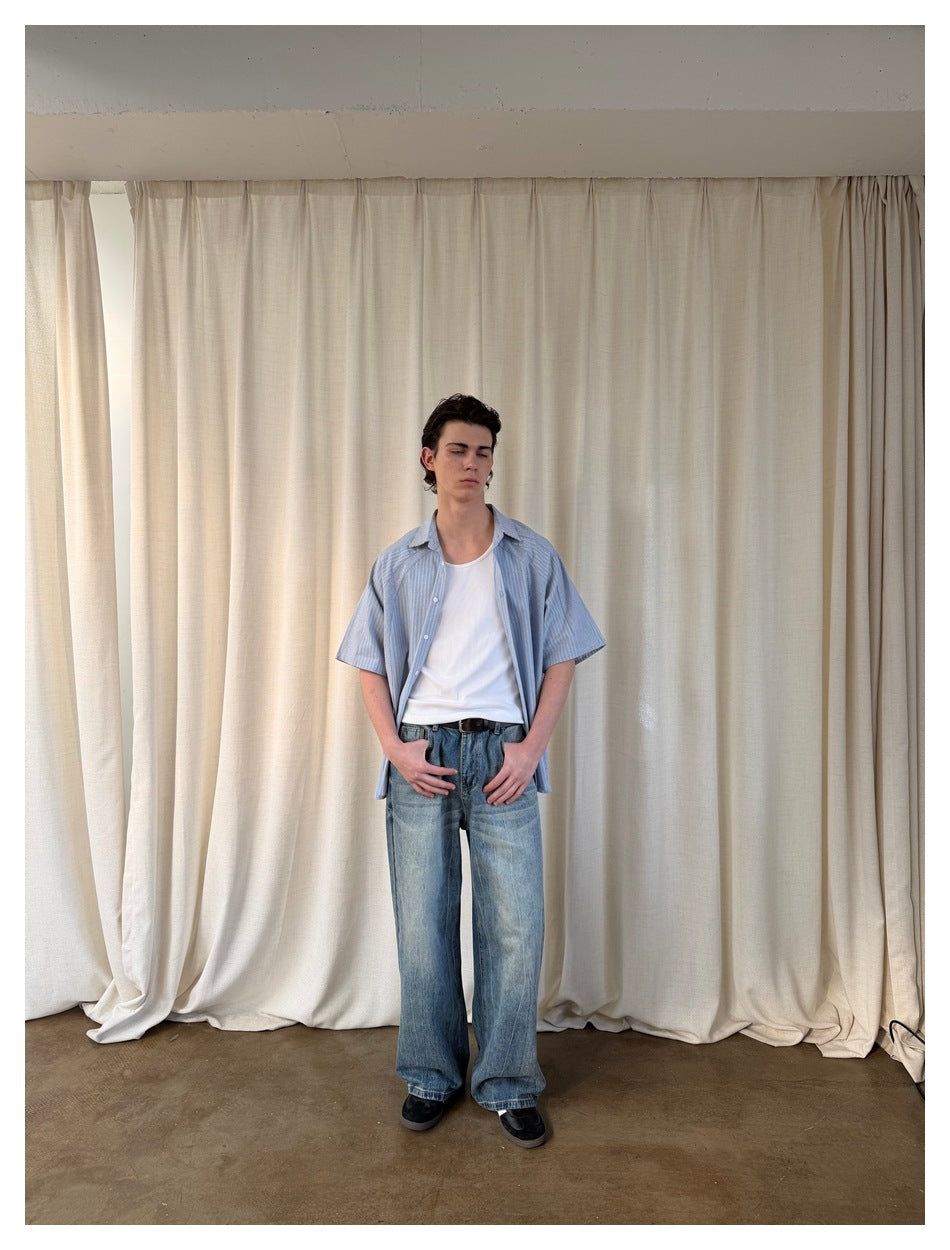 Front view of a model in an open blue striped short-sleeve shirt, white tank top, and loose blue jeans.