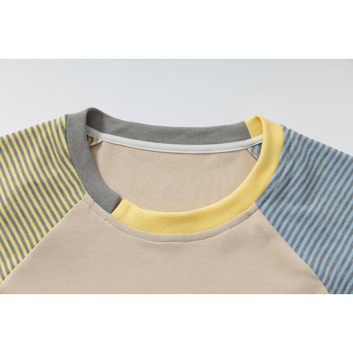 Close-up of a beige raglan shirt neckline with a yellow collar and gray-yellow and blue-gray striped sleeves.