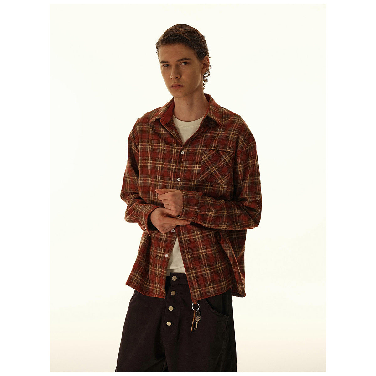 Model wearing a rust-red and brown plaid button-up shirt with a chest pocket, layered over a cream tee.