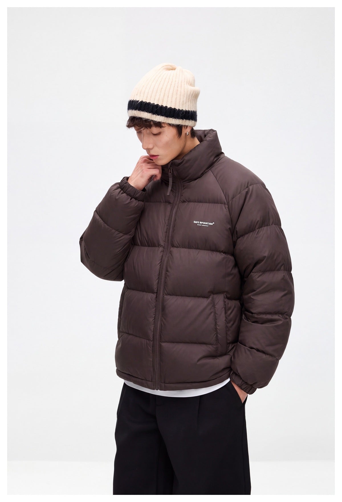 Model wearing a dark brown quilted puffer jacket with a high collar and a cream knit beanie.