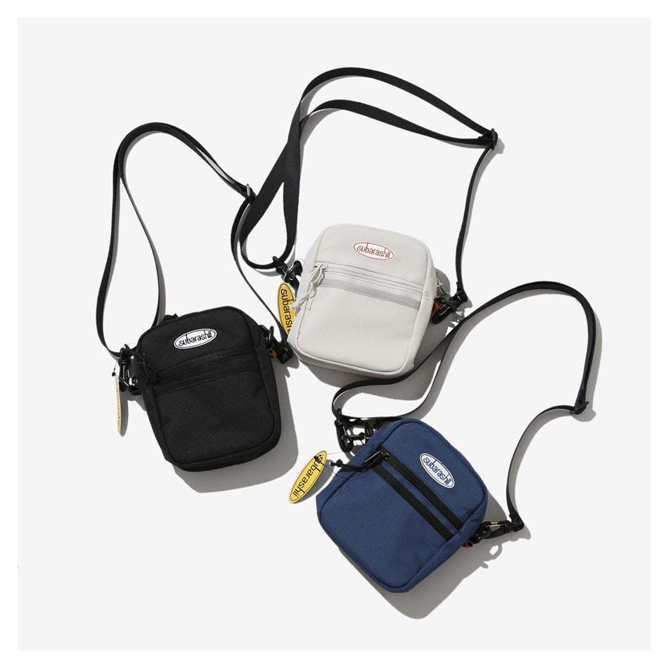 Three small crossbody bags in black, light gray and blue laid flat with black straps