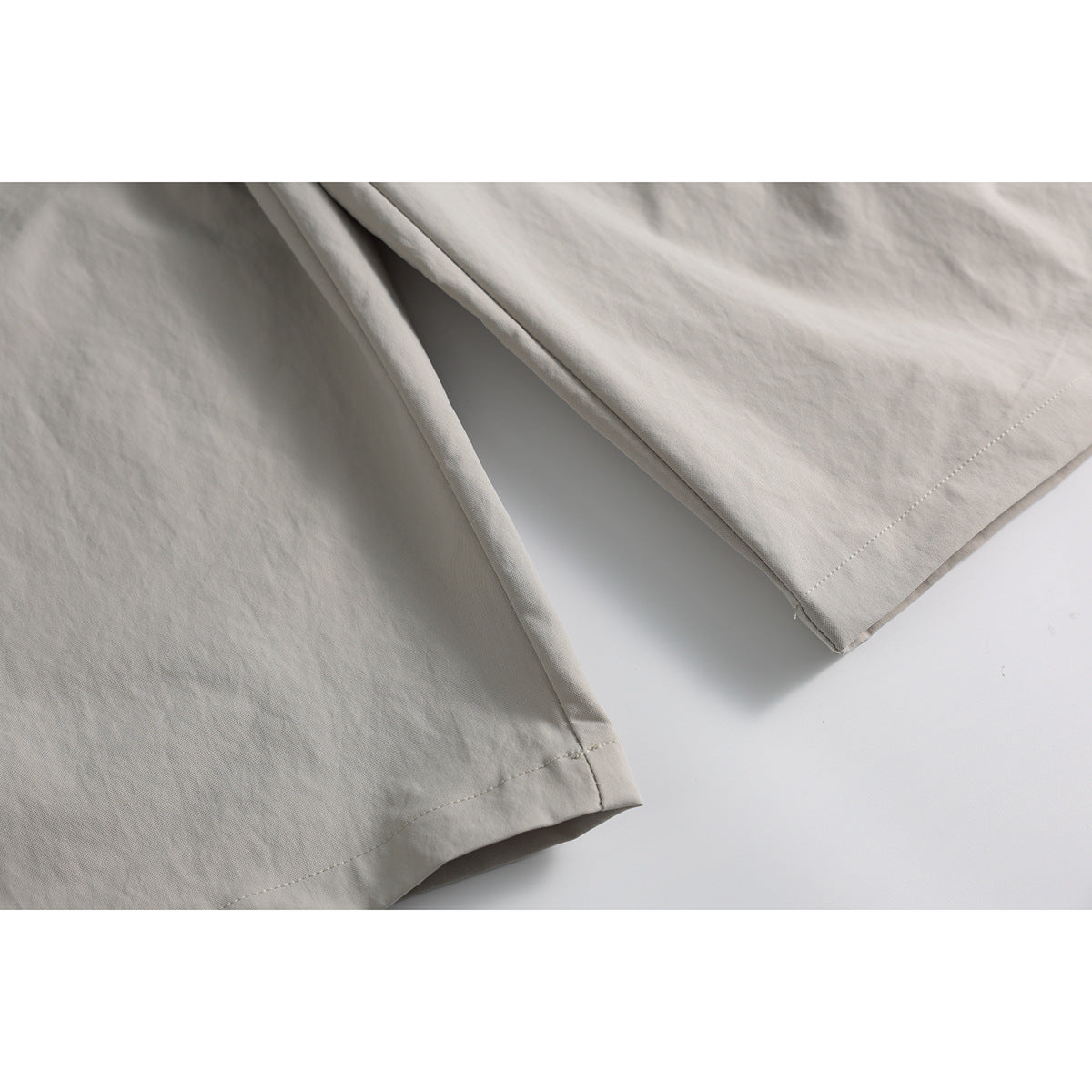 Close-up of the stitched hems and wide legs of light beige trousers.