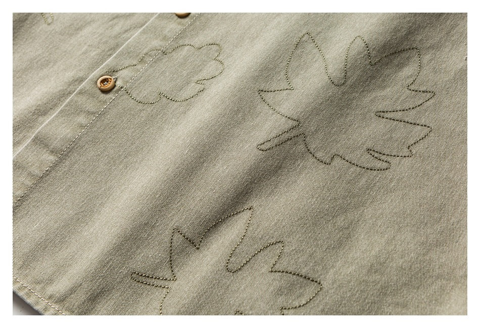 Close-up of a khaki-olive garment with outlined leaf stitching and a small tan button.