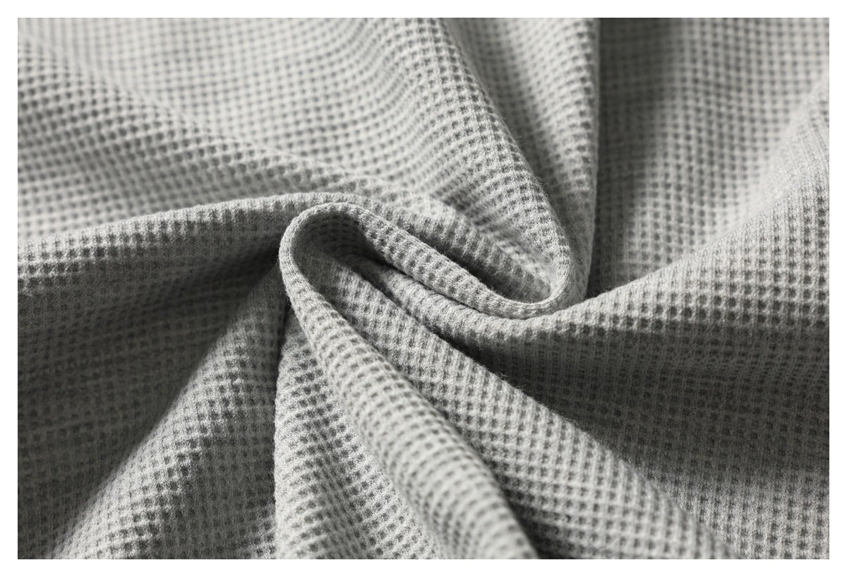 Macro view of light gray waffle-textured fabric folded into soft ripples.