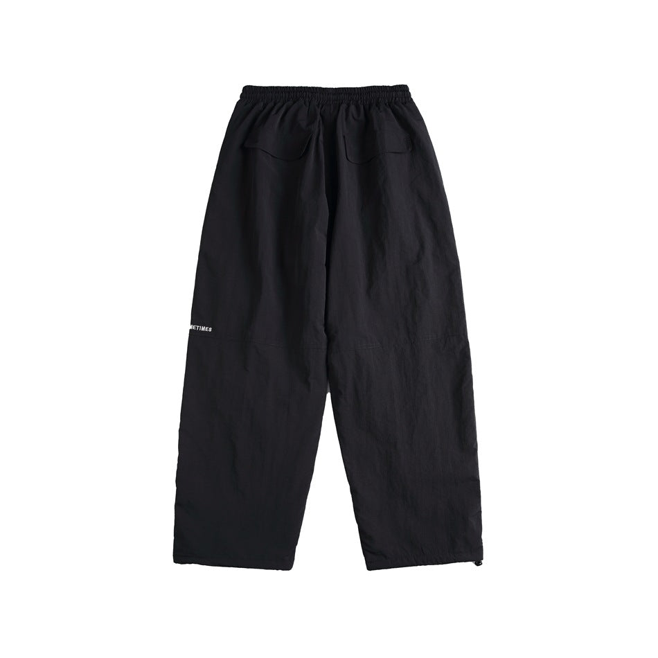 Black wide-leg pants back view with elastic waistband, two back flap pockets and small white leg text