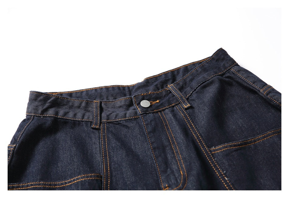 Close-up of the front waistband, button, belt loops and contrast-stitched seams on dark indigo denim shorts.