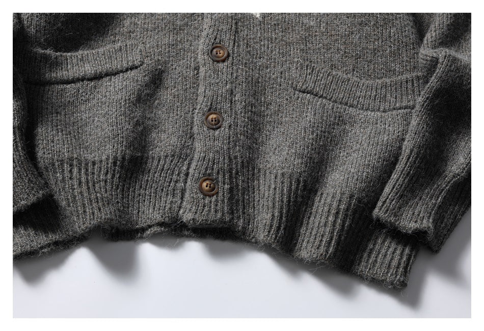 Close-up of a charcoal gray knit cardigan front with brown buttons, patch pockets, and ribbed hem and cuffs.