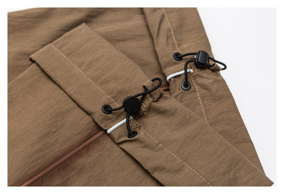 Close-up of brown trousers with black cord locks and adjustable drawcords at the waistband.