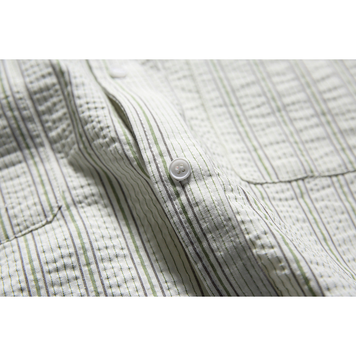 Close-up of the striped shirt's button placket and chest pocket, showing a white button and fine gray and green stripes.