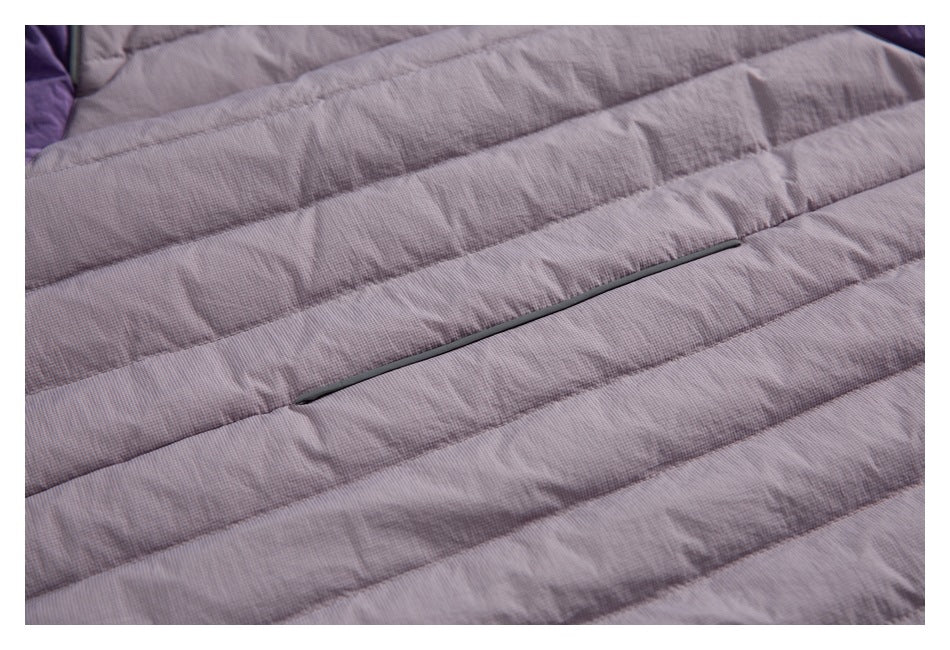 Close-up of a slim dark zipper set across the horizontal quilting of a mauve jacket.